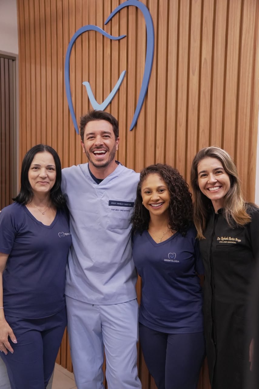 Dr. Virgílio, Dra. Raphaela e a equipe da VRClinica diante do logo da clínica.