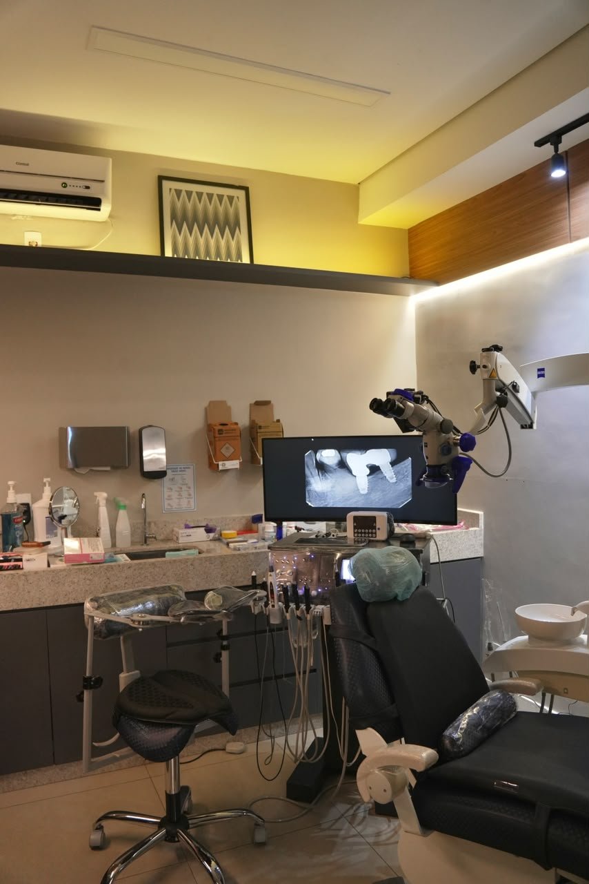 Sala clínica com monitor, cadeira odontológica e microscópio.