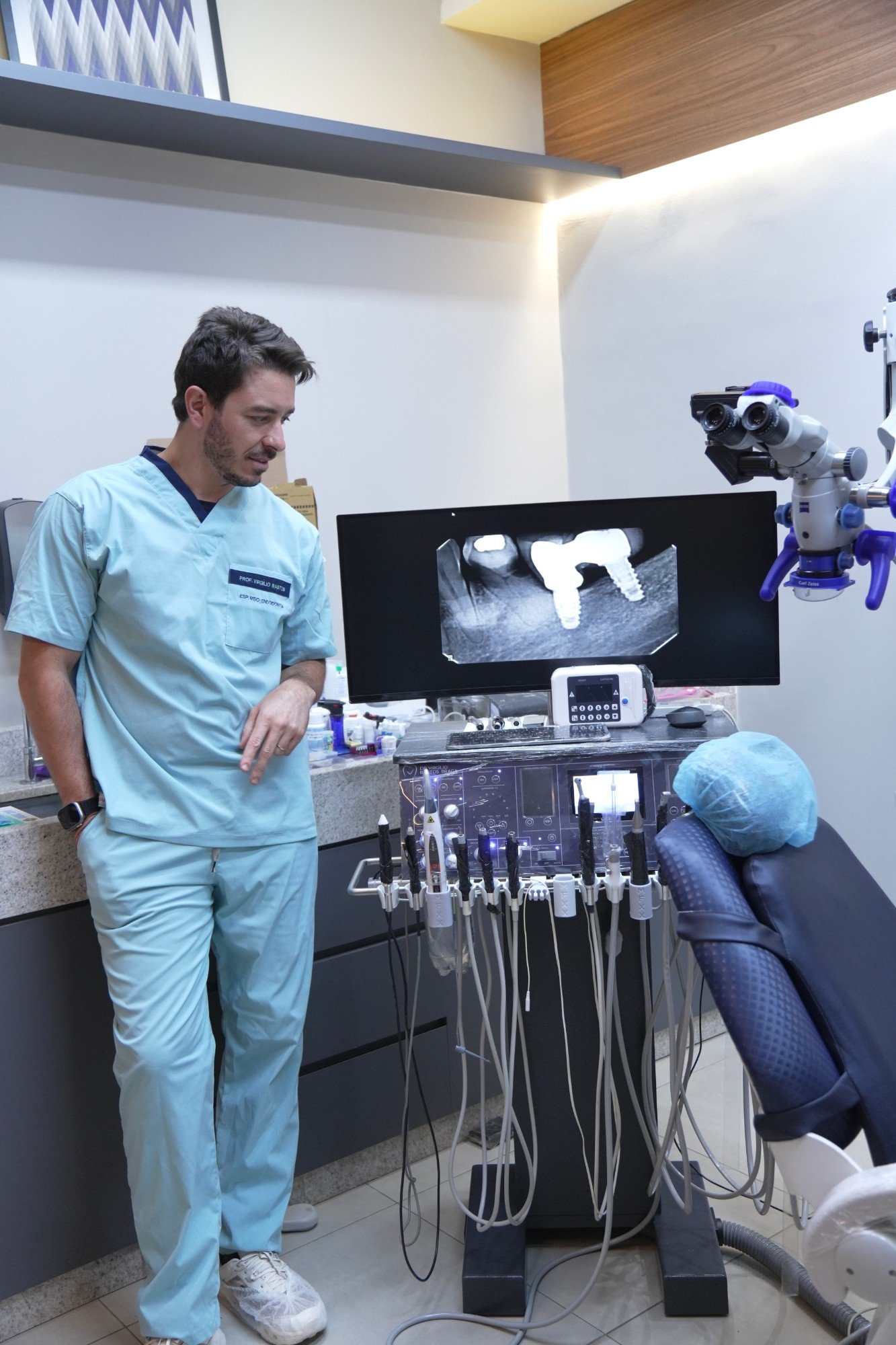 Dr. Virgílio ao lado dos equipamentos e da radiografia no monitor.